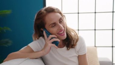 Evdeki kanepede oturmuş akıllı telefondan konuşan genç, güzel İspanyol kadın.