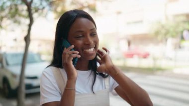 Genç Afrikalı Amerikalı kadın gülümsüyor. Kendine güveni tam. Sokakta akıllı telefondan konuşuyor.
