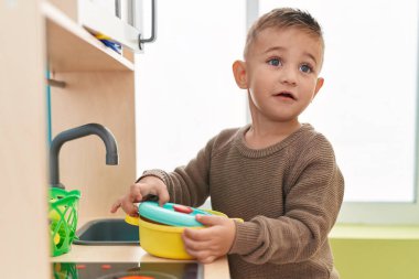 Adorable hispanic boy playing with play kitchen standing at kindergarten