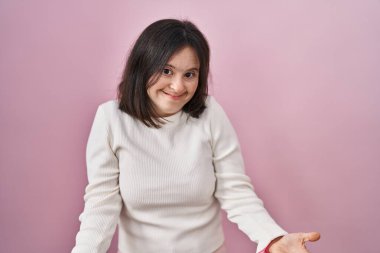 Woman with down syndrome standing over pink background clueless and confused with open arms, no idea concept. 