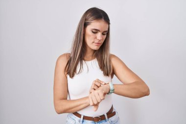 Hispanic young woman standing over white background checking the time on wrist watch, relaxed and confident 