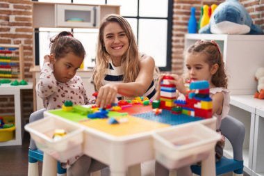 Teacher with girls playing with construction blocks sitting on table at kindergarten