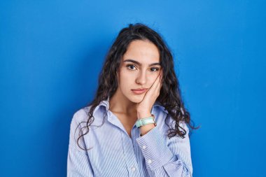 Mavi arka planda duran esmer kadın kollarını kavuşturarak depresyondan sıkılmış ve yorgun görünüyor.. 