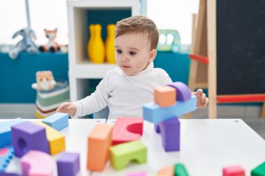 Sevimli beyaz bebek anaokulunda duran inşaat bloklarıyla oynuyor.