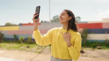 Genç Afro-Amerikalı kadın sokakta akıllı telefon kullanarak gülümsüyor.