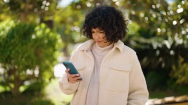 Young hispanic woman using smartphone with winner expression at park