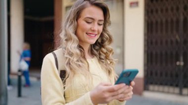 Young blonde woman tourist using smartphone walking at street