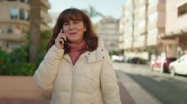 Middle age redhead woman smiling confident talking on the smartphone at street