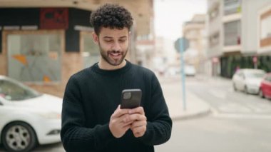 Genç Arap adam sokakta akıllı telefon kullanarak kendinden emin gülümsüyor.