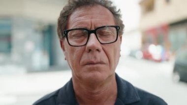 Orta yaşlı bir adam sokakta kendine güvenerek gülümsüyor.