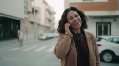 Orta yaşlı İspanyol kadın gülümsüyor. Akıllı telefondan konuşuyor.