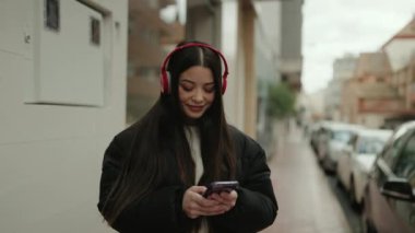 Genç İspanyol kadın sokakta akıllı telefon kullanarak müzik dinliyor.
