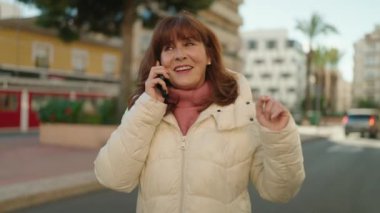 Middle age redhead woman smiling confident talking on the smartphone at street