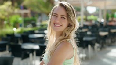 Young blonde woman standing with arms crossed gesture at coffee shop terrace