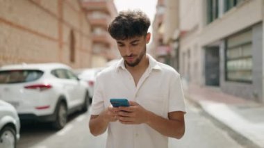 Young arab man smiling confident using smartphone walking at street