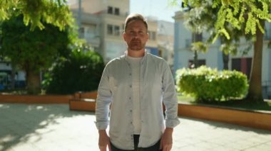 Parkta kendine güvenen beyaz bir adam gülümsüyor.
