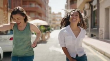 İki kadın anne ve kız gülümseyerek sokakta dans ediyorlar.