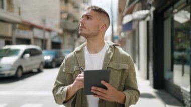 Young hispanic man smiling confident drawing on touchpad at street