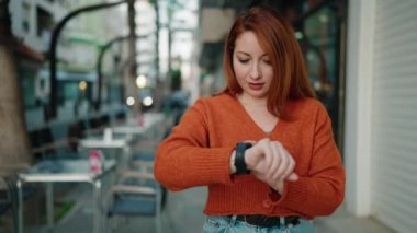 Young redhead woman smiling confident looking watch at street