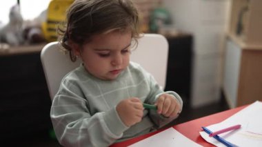 Anaokulunda masaya oturmuş kağıda resim çizen sevimli İspanyol kız öğrenci.