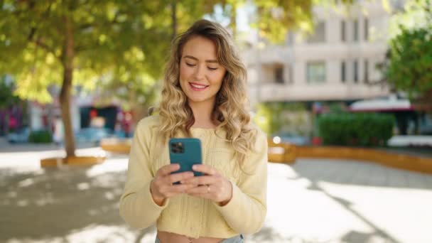 年轻的金发女人笑着自信地在公园的智能手机前自拍 — 图库视频影像