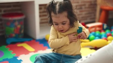 Adorable hispanic girl playing with maths puzzle game sitting on floor at kindergarten