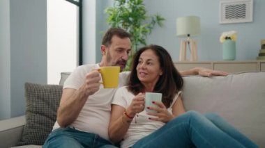 Man and woman couple drinking coffee using smartphone at home