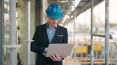 Young caucasian man architect with relaxed expression using laptop at street