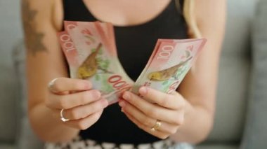 Young woman counting new zealand 100 dollars banknotes at home