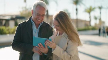 Middle age couple couple smiling confident using touchpad at park