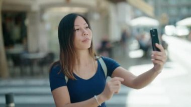 Young asian woman smiling confident making selfie by the smartphone at coffee shop terrace