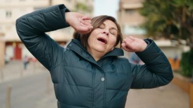 Middle age woman tired stretching arms at street