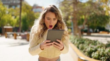 Young blonde woman using touchpad with winner expression at park