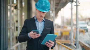 Young caucasian man architect using touchpad and talking on the smartphone at street