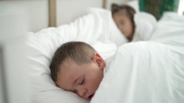 Adorable girl and boy lying on bed sleeping at bedroom