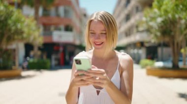 Genç sarışın kadın parkta akıllı telefon kullanıyor.