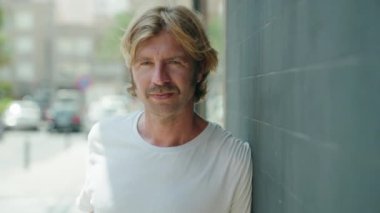 Sokakta kendine güvenen genç sarışın adam gülümsüyor.