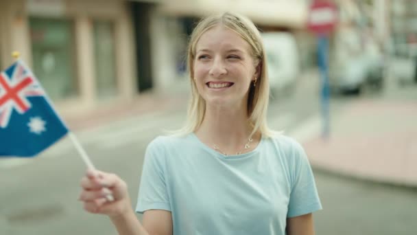年轻的金发女子带着自信的笑容在街上举着澳大利亚国旗 — 图库视频影像