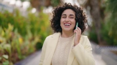 Parkta yürürken akıllı telefondan konuşan genç bir kadın.