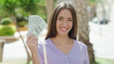 Young beautiful hispanic woman smiling confident holding dollars at street
