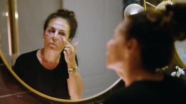 Middle age hispanic woman using makeup to cover signs of domestic violence at bathroom