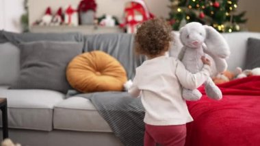 Adorable caucasian girl playing with toys sitting on sofa by christmas tree at home