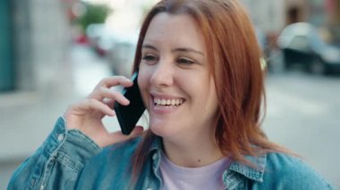 Genç, güzel, iri yarı, kendine güvenen bir kadın caddede akıllı telefondan konuşuyor.