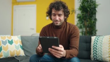 Genç İspanyol adam evdeki koltukta otururken dokunmatik ped kullanıyor.