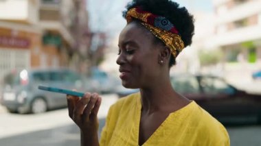 Genç Afrikalı Amerikalı kadın gülümsüyor. Kendine güveni tam. Sokakta akıllı telefondan konuşuyor.