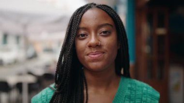 Afro-Amerikalı kadın gülümsüyor. Kollarını kavuşturup caddede duruyor.