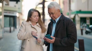 Middle age couple couple using smartphone and credit card at street