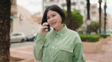 Genç Çinli kadın gülümsüyor caddede akıllı telefondan konuşuyor.
