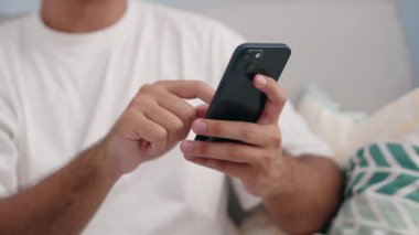 Young hispanic man using smartphone at home