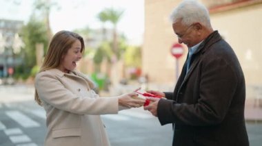 Middle age couple couple hugging each other holding birthday gift at street